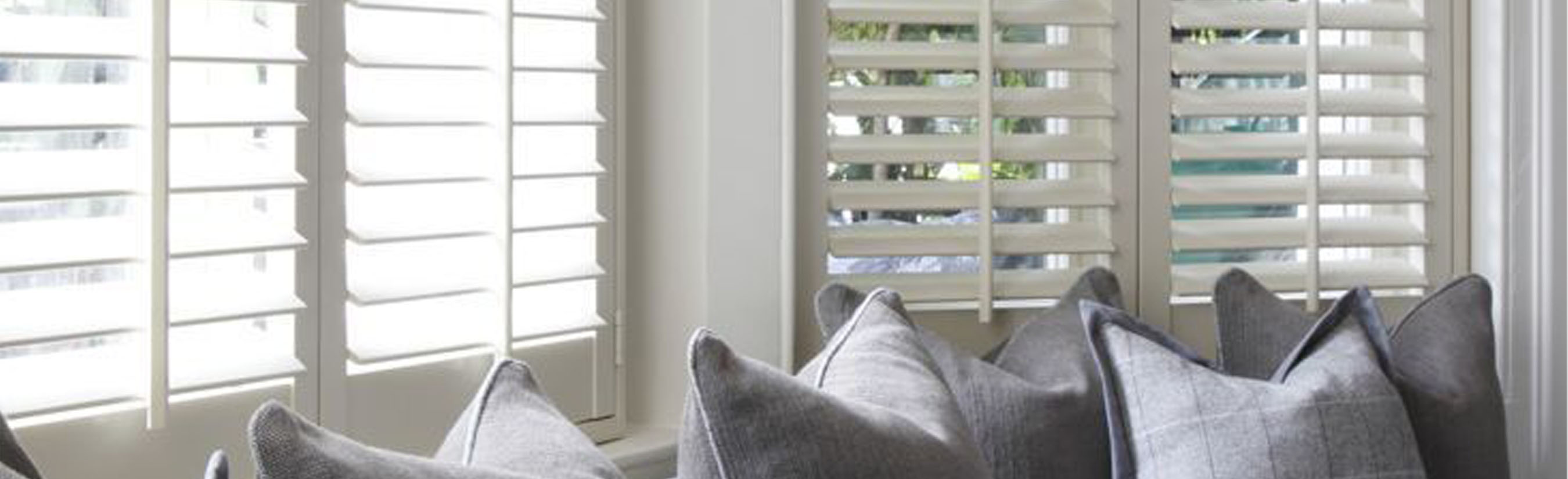 White polywood shutters by a long window seat with blue and white throw pillows.